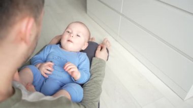 Baba, evde dizlerinin üzerine çökmüş gülümseyen bir bebekle oynuyor..