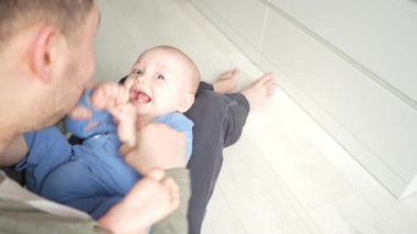 Baba, evde dizlerinin üzerine çökmüş gülümseyen bir bebekle oynuyor..