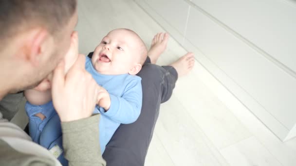 Padre juega con un hijo sonriente acostado de rodillas en casa juntos. — Vídeo de stock