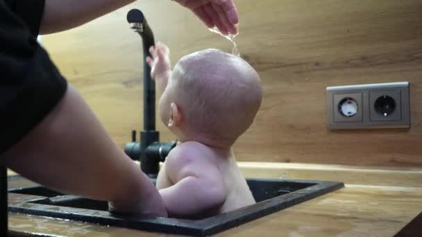 Bebé en fregadero de cocina bañándose y jugando con agua. — Vídeos de Stock