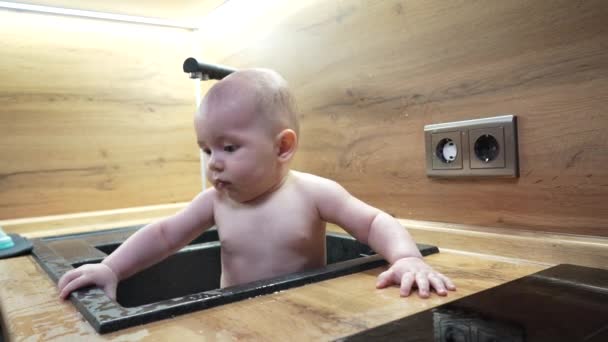 Bebé en fregadero de cocina bañándose y jugando con agua. — Vídeo de stock