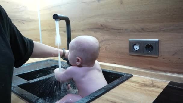 Bayi di wastafel dapur mandi dan bermain dengan air. — Stok Video