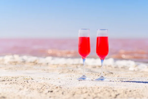 Two glasses with a pink drink on the shore of a pink lake. A romantic setting for lovers. Selective focus