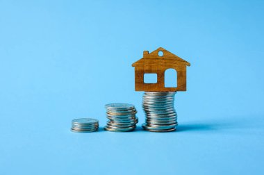 Bozuk para yığınının üzerinde duran küçük bir ev figürü. Bir ev satın almak için tasarruf kavramı.