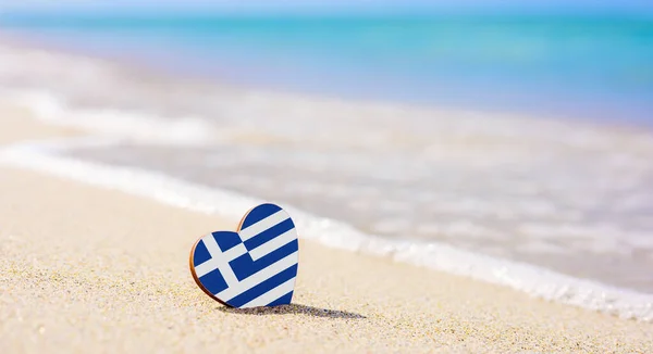 Kumlu bir plajda kalp şeklinde Yunanistan bayrağı. Yunan tatil beldelerindeki en iyi tatil kavramı