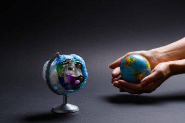 Karanlık bir arka planda çöpten yapılmış bir dünya. Arka planda, kadınların elinde temiz bir gezegen var. Dünyaya seçici odaklanma