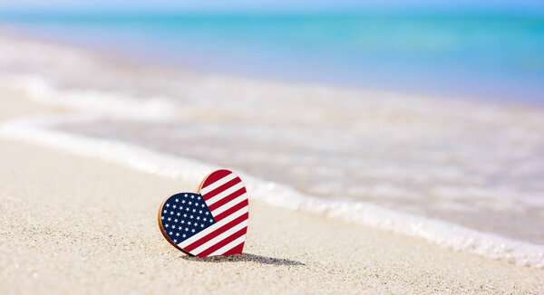 Flag of the USA in the shape of a heart on a sandy beach. The concept of the best vacation in USA