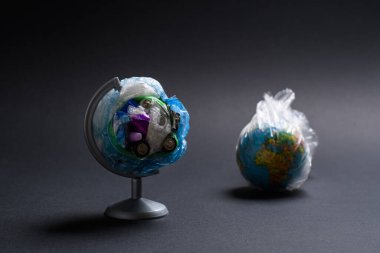 Plastikten kaynaklanan çevresel felaket kavramı. Gezegenin arka planındaki çöplerden oluşan dünya karanlık bir arka planda bir paketin içinde. Çöpten yapılmış bir küreye seçici odaklanma.