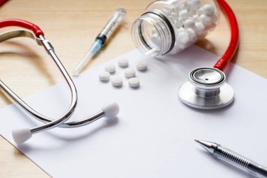 Klinikte doktor randevusu. Teşhisi kaydetmek için beyaz bir çarşafa tıbbi malzemeler ve ilaçlar. Kalemin ön planına seçici odaklanma.