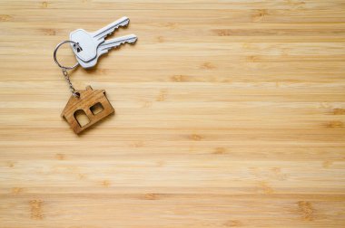 Ahşap bir arka planda ev şeklinde anahtarlığı olan yeni bir evin anahtarları..