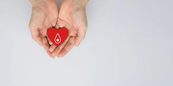 Blood donation concept. Red heart with a drop of blood in the hands. Copy space.