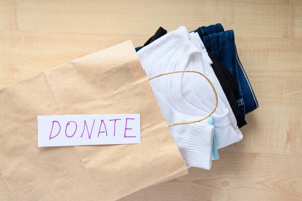 Clothes for donation and aid in paper craft bag. The concept of donating and helping people in need. Selective focus, top view.