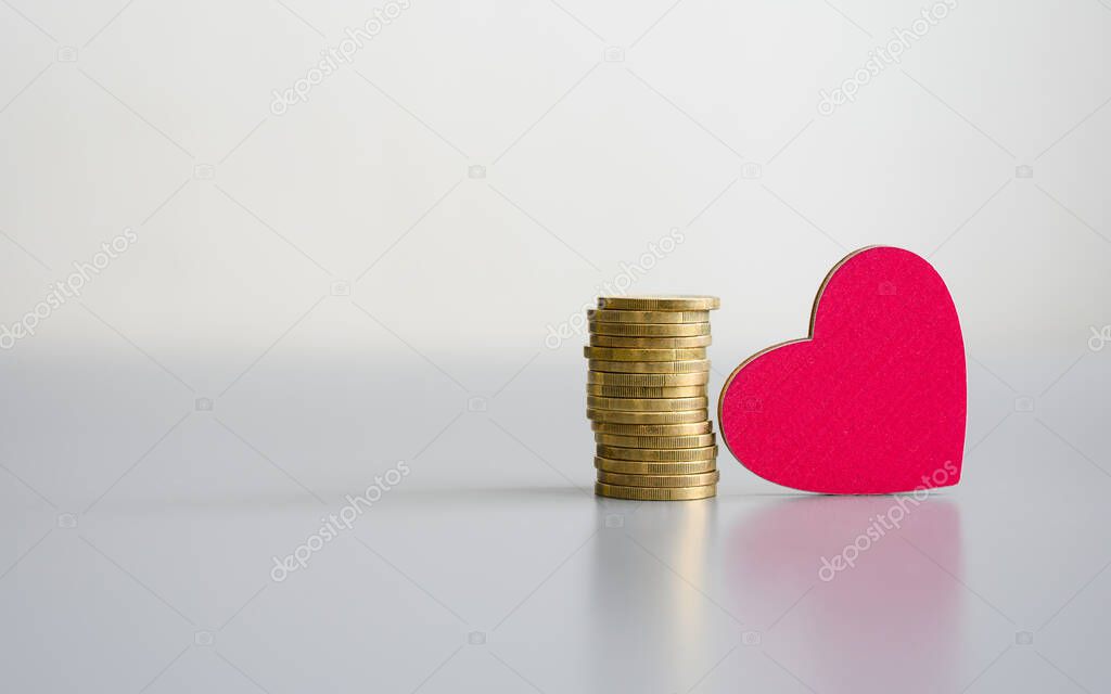 Stack of coins and a wooden red heart on a gray background. Donation concept.