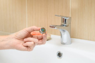 A man's hand shows a dirty filter from a water faucet in the bathroom. Lots of sandy sediment in running water. Selective focus on the filter.