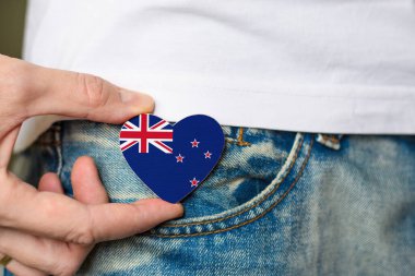 Resident of New Zealand. Wooden badge with New Zealand flag in the shape of a heart in a man's hand.
