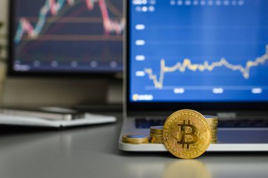 Bitcoin income growth concept. Bitcoin coin against the background of growing income graphs on monitors. Selective focus on bitcoin.