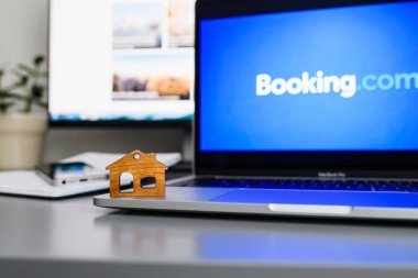 Vladimir, Russia - January 2022: Figurine of a wooden house on a laptop against the background of the Booking website. The concept of online housing search. Selective focus on the house.
