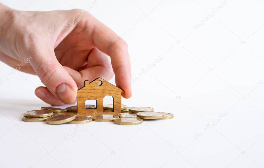 A man's hand puts a small wooden house on a pile of coins. Real estate purchase concept.Selective focus on the house.