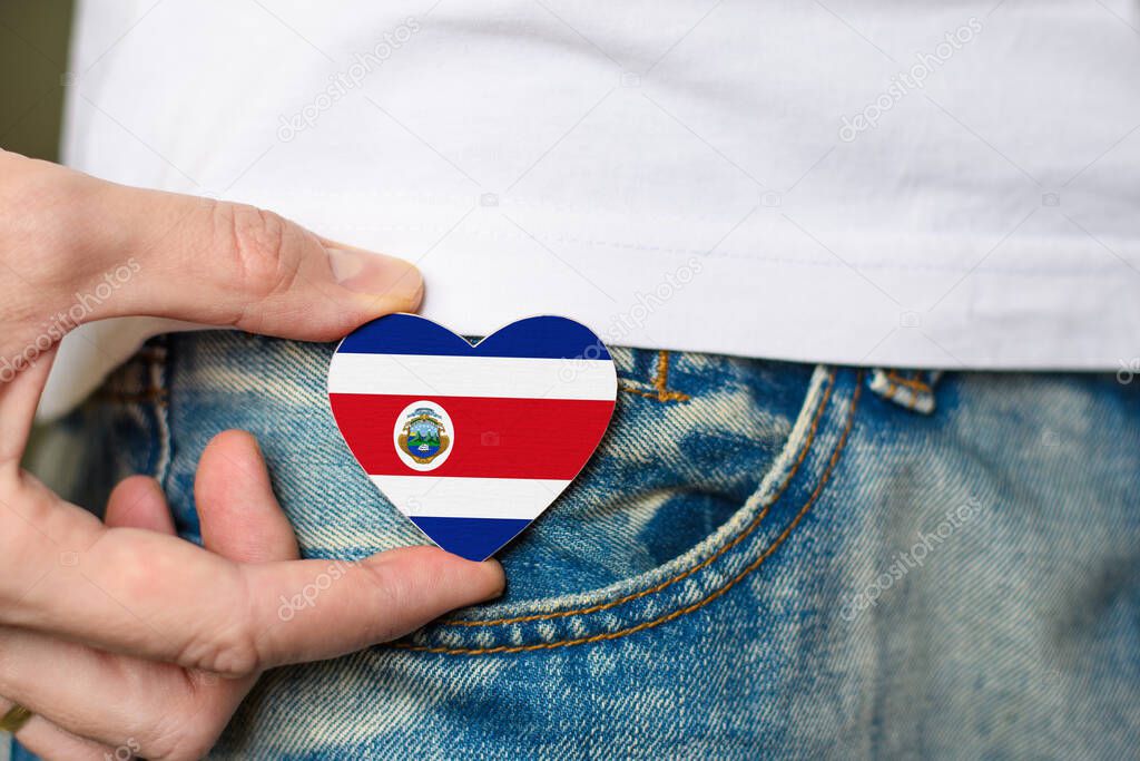 Resident of Costa Rica. Wooden badge with Costa Rica flag in the shape of a heart in a man's hand.