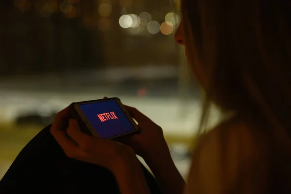 ロシアのウラジミール 1月2022 スマートフォンの窓の上の夜の女の子は Netflixシリーズを見るためのアプリケーションを開きます ロゴの選択的フォーカス ストック画像