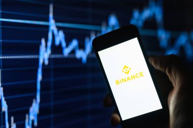 Vladimir, Rusya - Ocak 2022: Benance kripto döviz alım-satım uygulaması bir akıllı telefon üzerinden karanlıkta grafiklerin arka planına karşı. Logoya seçici odaklanma.