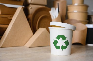 Ekolojik aletlerin arka planında yeşil geri dönüşüm sembolü olan beyaz plastik bir kap ya da cam. Üretim için ayrıştırılabilir materyaller kullanma kavramı. Seçici odak.