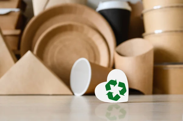 A figurine of a heart with a green recycle sign on the background of disposable biodegradable tableware. The concept of environmental protection.