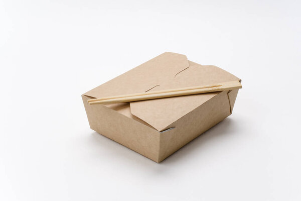 Chopsticks on a closed cardboard box for food delivery on a white background. Rectangular eco-friendly dishes for the delivery of Asian cuisine. Template for advertising.