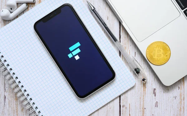 Vladimir, Rusya - Şubat 2022: FTX kripto para birimlerini bir dizüstü bilgisayar ve bir bitcoin 'in yanındaki akıllı telefondan satma başvurusu. Yukarıdan görüntüle.