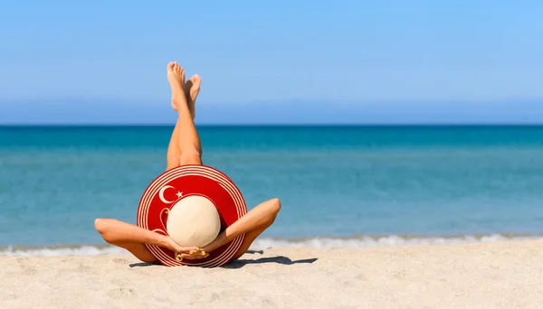 トルコの旗の色でわらの帽子のビーチで細い日焼けした女の子 トルコのリゾート地での完璧な休暇の概念 帽子に集中しろ — ストック写真