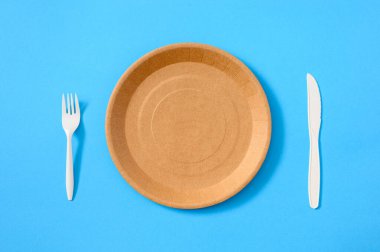 Boş kağıt tek kullanımlık tabak ve çatal ve mavi arka planda bıçak. Çevre dostu sofra takımı kullanımı. Yemek servisi. Yukarıdan görüntüle
