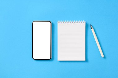 Beyaz ekranlı akıllı bir telefon ve mavi kağıt kaplamalı kalemli bir not defteri. Yat yere, maket yap.