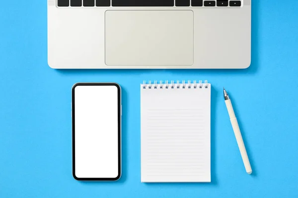 ノートパッドと青い紙の背景にノートパソコンのキーボードと空白の画面のスマートフォンのトップビュー フラットレイアウト コピースペース モックアップ — ストック写真