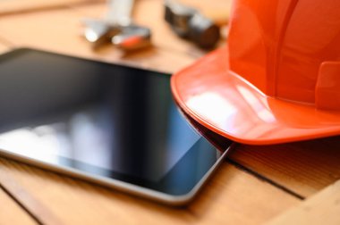 Tablet ve inşaat miğferi yakın plan. Defocus, kaskın güneşliğine odaklan. İnşaat konsepti.