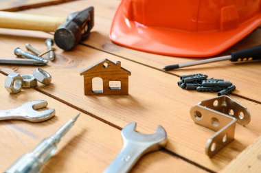 İnşaat aletleri ve sert bir şapka ahşap bir masanın üzerindeki küçük bir ev heykelinin etrafında duruyor. Seçici bir şekilde eve odaklan. İnşaat ve onarım kavramı.