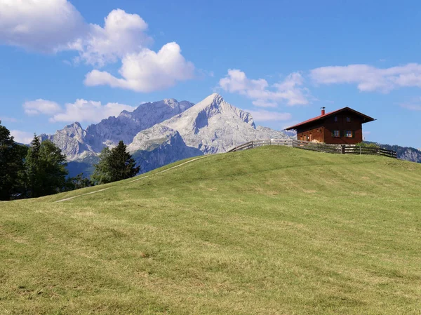 Dağ çayırında kulübesi ve arka planda dağları var.