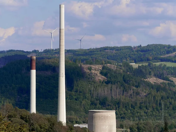 In the foreground a decommissioned coal-fired power plant, in the background wind turbines.