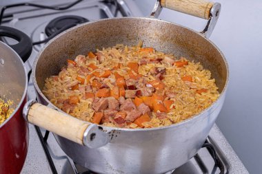 brown rice with pieces of carrot and pepperoni sausage cooking in the pan