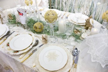 Yılbaşı yemeği. Güzel servis edilmiş bir masa. Beyaz çanak çömlek ve dantel masa örtüsü. Temiz çatal bıçak takımı.