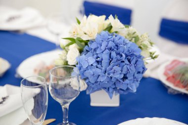 Cam vazoda bir buket beyaz ve mavi çiçek. Masanın üzerinde mavi ortanca var. Yemek masasının dekorasyonu. Tatil için çiçekler..