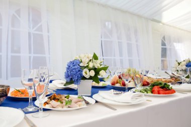 Akşam yemeği için dekore edilmiş masa hazır. Yemek masasında bir buket çiçek. Düğün için çiçekler, tabaklar ve peçetelerle süslenmiş güzel bir masa ya da restoranda başka bir etkinlik.