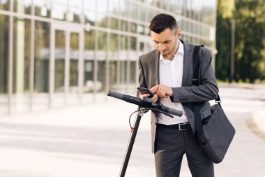 İşadamı e-scooterına doğru yürüyor. Turist park alanında elektrikli scooter kullanıyor. Çevre dostu ulaşım. Yetişkin bir adam işe elektrikli scooterla gidiyor.