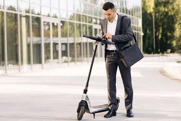 Omul folosește un scuter electric ca mijloc modern de transport în oraș. Un om de afaceri de sex masculin se apropie de un scuter electric și utilizează aplicația telefonului mobil. Transportul ecologic — Fotografie, imagine de stoc