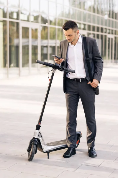 Un om de afaceri de sex masculin se apropie de un scuter electric și utilizează aplicația telefonului mobil. Transport ecologic. Omul folosește un scuter electric ca mijloc modern de transport în oraș — Fotografie, imagine de stoc