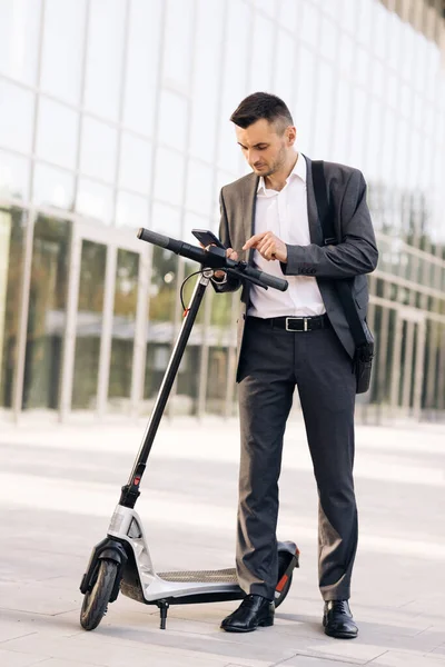 Telefonní aplikace pro půjčovnu skútrů. Ekologická městská doprava. Podnikatel pronajímá elektrický skútr pomocí aplikace pro mobilní telefon. Člověk si vezme elektrický koloběžku. Turistická jízda e-scooter nebo na kole — Stock fotografie