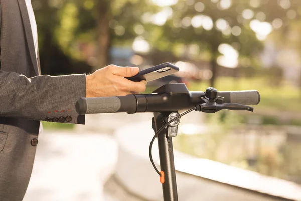 Turista llevar scooter eléctrico en el estacionamiento compartido. Transporte ecológico. Hombre guapo en un traje montando scooter eléctrico para trabajar. Empresario caminando hacia su e-scooter — Foto de Stock