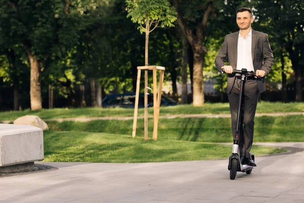 Jonge zakenman op een elektrische scooter voor een zakelijke bijeenkomst in het kantoor, kantoorgebouwen, zakenman, elektrisch transport, ecologisch transport, e-skateboard. Milieuvriendelijk vervoer — Stockfoto