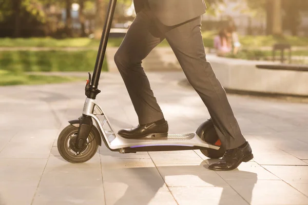 Primer plano de las piernas hombre en traje de montar scooter eléctrico en la ciudad. Hombre de negocios desconocido en traje clásico paseo en scooter móvil eléctrico. Moderno transporte ecológico. Transporte eléctrico de conducción rápida — Foto de Stock