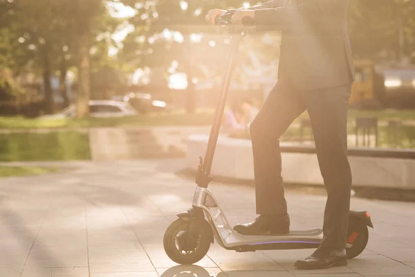 Ismeretlen üzletember, klasszikus öltönyben, elektromos robogóval. Közelkép lábakról öltönyös férfi elektromos robogóval a városban. Modern környezetbarát közlekedés. Villamos gyorshajtás — Stock Fotó