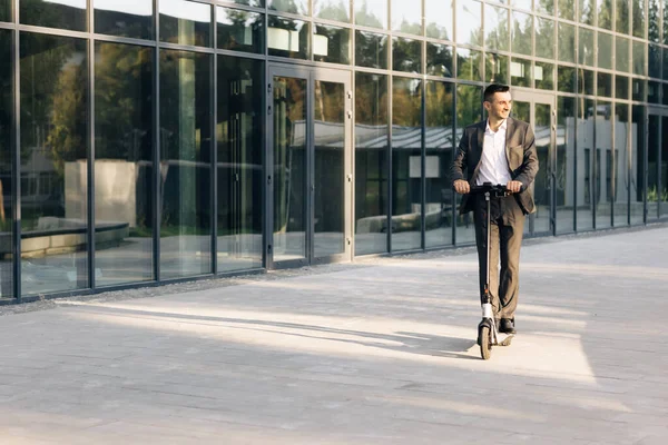 Handsome man in a suit riding electric scooter in a city. Adult businessman riding with electric scooter to work. Man rides an electric scooter on the road. Modern way of getting around